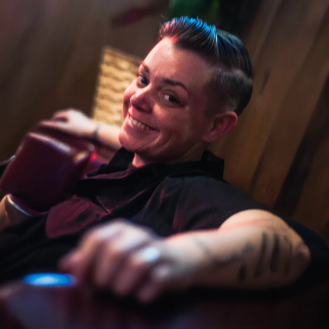 Candid photo of Jovi Radtke smiling while seated in a relaxed setting with colorful ambient lighting