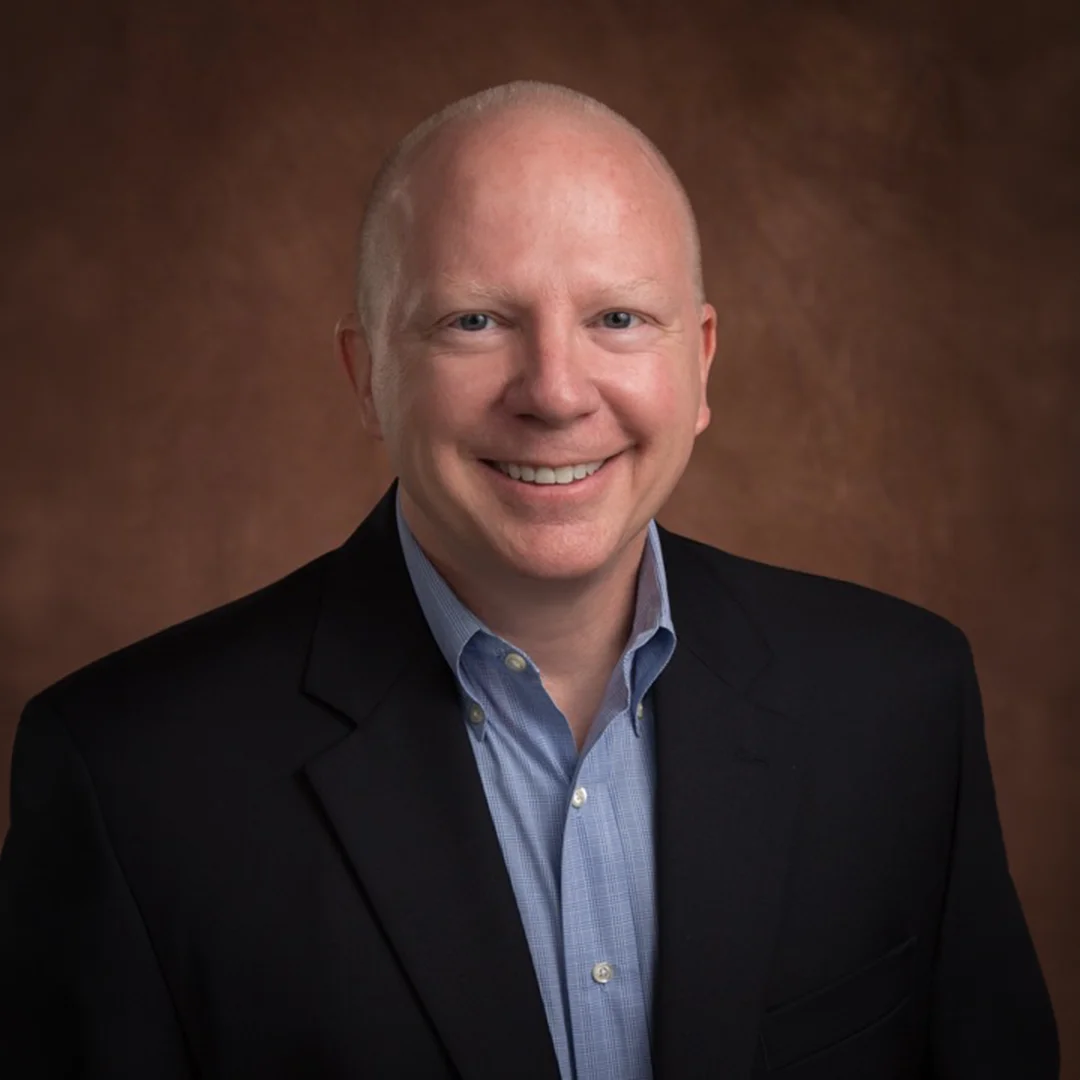 Professional headshot of Michael O’Donahue smiling in a suit jacket against a neutral studio background